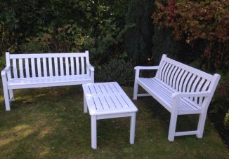 Newly painted slatted garden benches and small table with a white frame and seat. The benches are made of wood and they have a simple, yet elegant design. It is perfect for relaxing in the garden or reading a book outdoors.